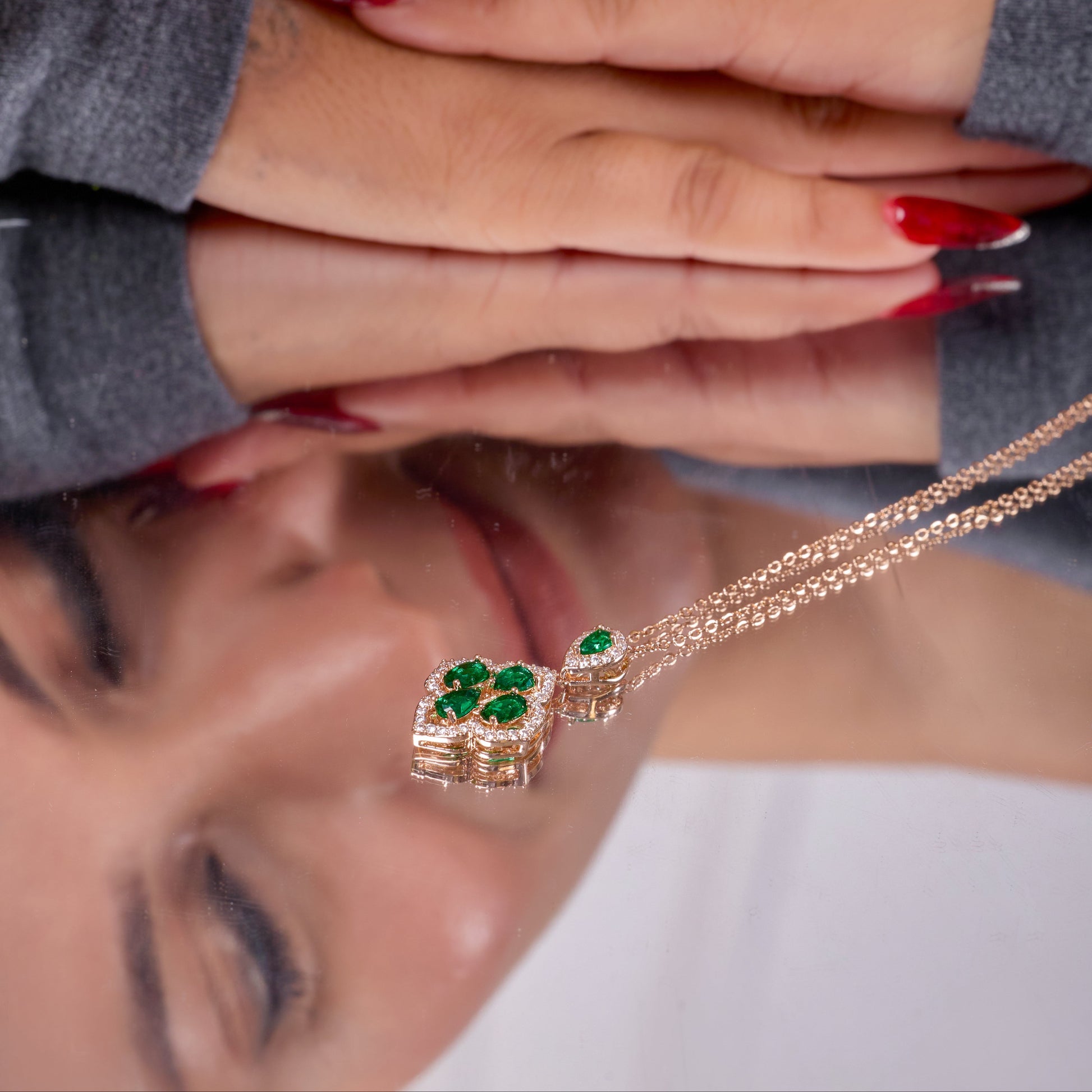 Close-up of a woman's face with a necklace featuring green gemstones, reflected on a surface.