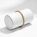 Gold and pearl bracelet on a white cylindrical stand against a light gray background