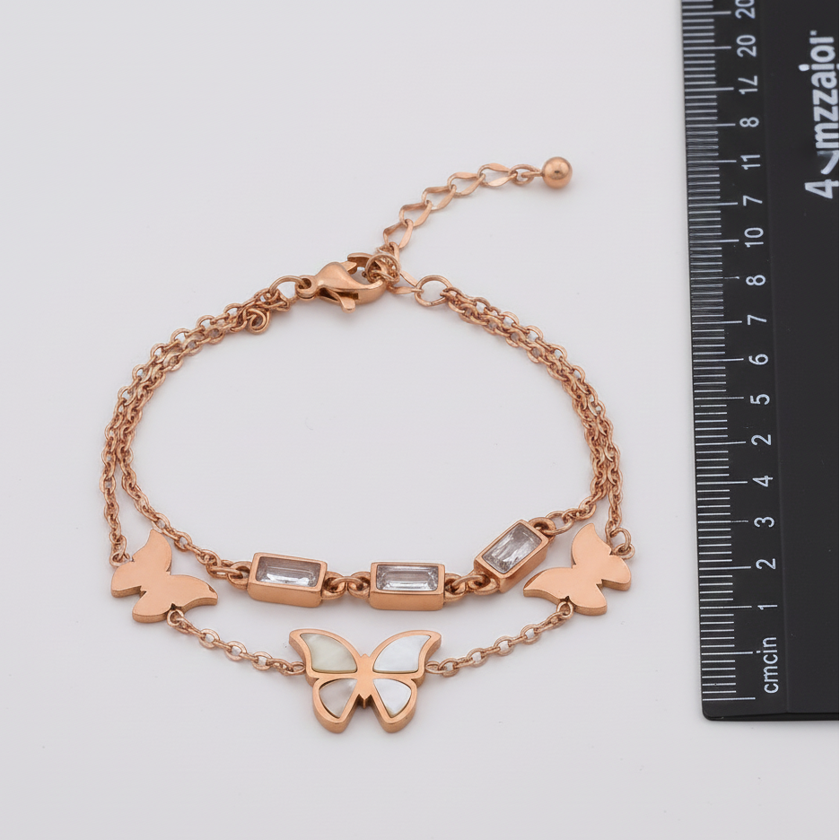 Rose gold bracelet with butterfly and rectangular charm on a white background with a ruler for scale.